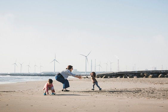 Asian family playing in the beach where there is wind power station in the background.