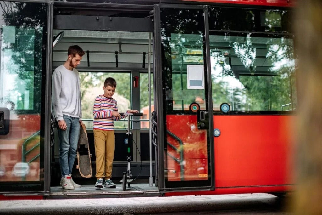 Adult and a young boy standing in the open door of a bus