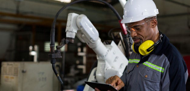 Industrial worker operating a robotic arm, highlighting the integration of AI intelligence with physical manufacturing operations.