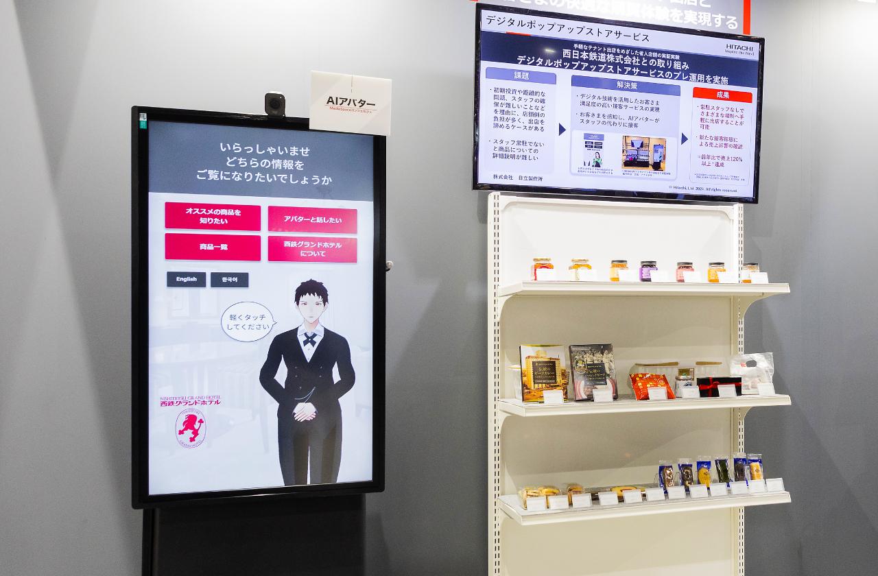 画像: 「リテールテックJAPAN 2024」にて日立が展示した、「デジタルポップアップストア」。左のデジタルサイネージに表示されたAIアバター「MediaSpaceコンシェルジュ」が接客を代行する