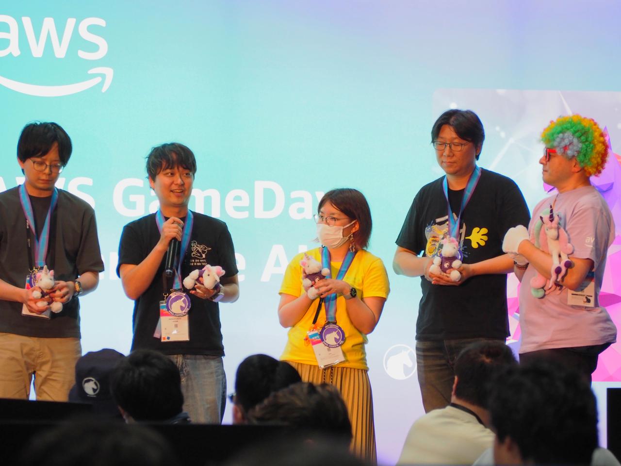画像:みごと優勝を勝ち取った「Team ECS」 左から2番目、マイクを持つ日立の小林直樹さん。