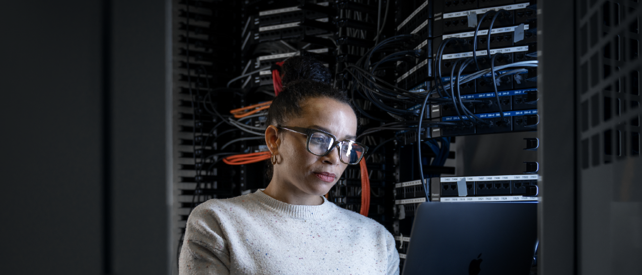 Woman standing in front of a data center rack holding a laptop